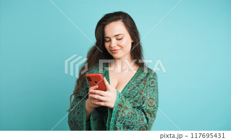Happy young woman using smartphone in blue studio 117695431