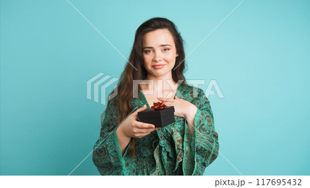 Happy young woman receiving gift box in blue studio 117695432