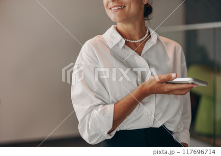 A Professional Woman Holding a Smartphone While in a Modern Office Setting and Environment 117696714