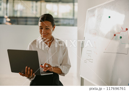 A skilled professional woman is diligently working on her laptop in a contemporary office setting 117696761