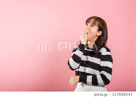 Portrait Asian beautiful young woman emotions tired and sleepy her yawning covering mouth open by hand, studio shot isolated on pink background, Thai female insomnia concept with copy space 117699241