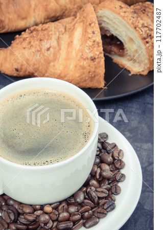Breakfast consisting of fresh croissant with chocolate and coffee in white cup 117702487