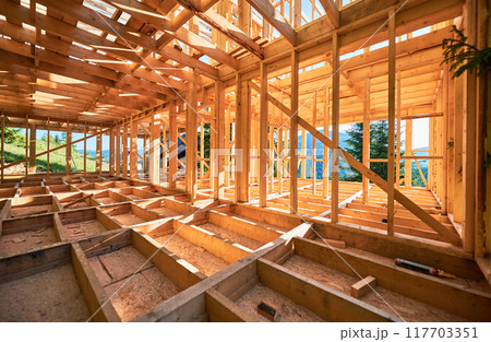 Under-construction residential wooden frame home located near a forest. Commencement of a new construction project for a cozy house or a mountain cottage. Idea of contemporary ecological construction. 117703351