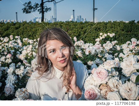 Young woman surrounded by blooming white roses enjoying nature in a beautiful garden Young woman surrounded by blooming white roses enjoying nature in a beautiful garden 117706198