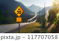 A high-speed highway in a picturesque mountainous area. There is a road sign on the side of the road warning about the speed limit 117707058