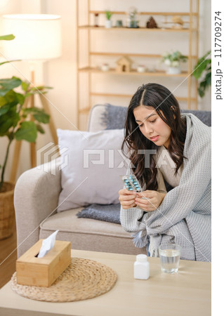 A woman is sitting on a couch with a box of tissues and a bottle of water A woman is sitting on a couch with a box of tissues and a bottle of water 117709274