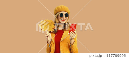 Autumn outfit, portrait of fashionable smiling young woman with phone holds yellow maple leaves Autumn outfit, portrait of fashionable smiling young woman with phone holds yellow maple leaves 117709996