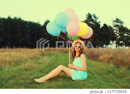 Happy cute smiling young woman with bunch of colorful balloons wearing dress outdoors Happy cute smiling young woman with bunch of colorful balloons wearing dress outdoors 117710010