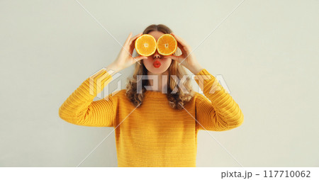 Summer portrait of happy cheerful woman covering eyes with slices of orange looking for something 117710062