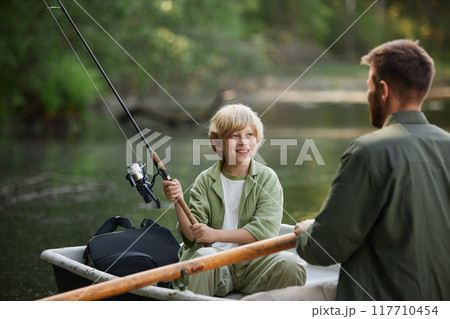 Child and adult enjoying peaceful fishing session on calm lake from small boat while child holding fishing rod having conversation in relaxed setting Child and adult enjoying peaceful fishing session on calm lake from small boat while child holding fishing rod having conversation in relaxed setting 117710454
