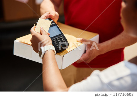 Close-up of person's hands conducting credit card payment transaction using card reader with box on counter, wearing white smartwatch on wrist, illustrating modern retail exchange Close-up of person's hands conducting credit card payment transaction using card reader with box on counter, wearing white smartwatch on wrist, illustrating modern retail exchange 117710608