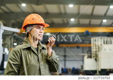 Wearing Hard Hat and Holding Walkie-Talkie in Factory Wearing Hard Hat and Holding Walkie-Talkie in Factory 117710702