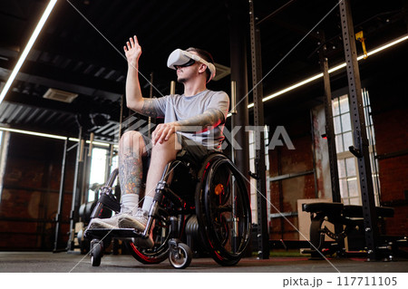 Side view portrait of young man with disability using wheelchair in gym and interacting with virtual objects using AR technology Side view portrait of young man with disability using wheelchair in gym and interacting with virtual objects using AR technology 117711105