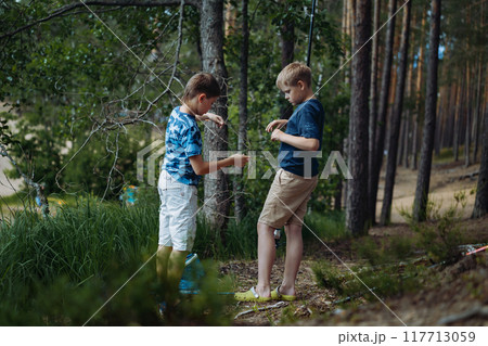 boys fishing by the lake in forest trying to untwine knot of fish wire boys fishing by the lake in forest trying to untwine knot of fish wire 117713059