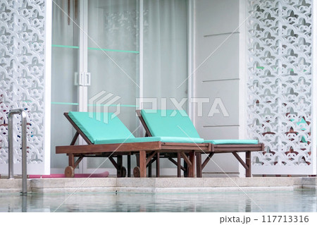 Wooden loungers with soft mattresses in pastel color by swimming pool 117713316