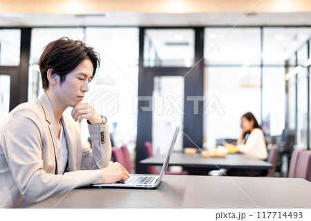 共用スペースでノートパソコンを使用して仕事をする男性 117714493