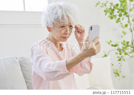 スマートフォンを見る老眼のシニア女性 117715551