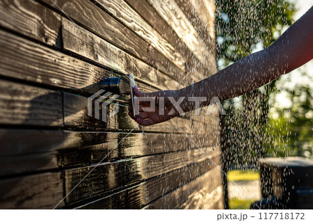 Female hand opens outdoor shower faucet at sunset. Concept of summer fun and relaxation with flowing water 117718172