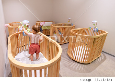 Joyful Toddler Standing in Crib in Contemporary Nursery. Concept of playful interaction and learning in daycare Joyful Toddler Standing in Crib in Contemporary Nursery. Concept of playful interaction and learning in daycare 117718184