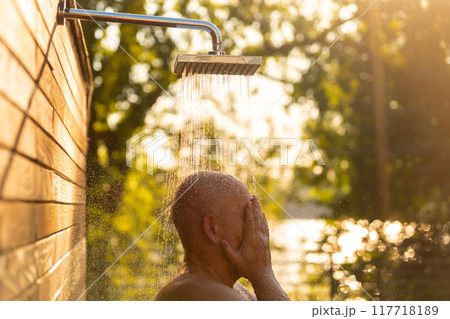 Man enjoying outdoor shower at sunset. Concept of evening relaxation and natural refreshment 117718189