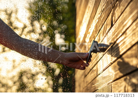 Female hand turns outdoor shower faucet at sunset. Concept of summer fun and refreshing shower with flowing water 117718313
