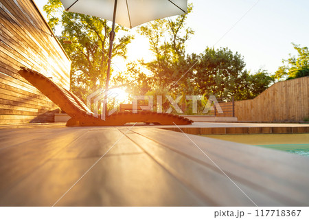 Elegant Wooden Lounge Chairs with White Umbrella at Poolside During Sunset. Concept of luxury and comfort in a serene outdoor setting 117718367