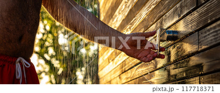 Panorama of a man opening outdoor shower at sunset. Concept of summer rest, fun, and refreshing with flowing water Panorama of a man opening outdoor shower at sunset. Concept of summer rest, fun, and refreshing with flowing water 117718371