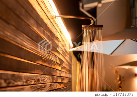 Outdoor shower with flowing water at night near swimming pool. Concept of refreshing showering before and after swimming 117718375