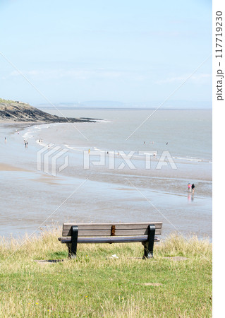 遠浅の砂浜を見下ろす丘に作られた木製のベンチと遠くに見える街並み　南ウェールズの郊外にて 117719230