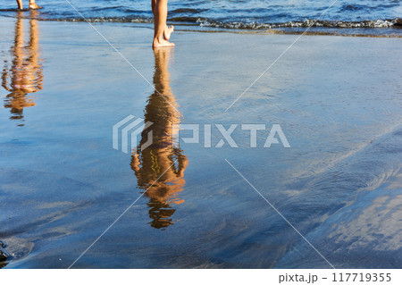 Reflections of the two female figures in the wet coast. Two female figures are reflected in the wet sand prebrezhnogo Reflections of the two female figures in the wet coast. Two female figures are reflected in the wet sand prebrezhnogo 117719355