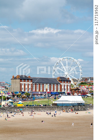遠浅の砂浜の海岸でくつろぐ人々と海岸沿いの遊園地 南ウェールズの郊外にて 遠浅の砂浜の海岸でくつろぐ人々と海岸沿いの遊園地 南ウェールズの郊外にて 117719562