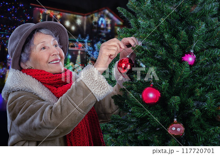 Festive Spirit Alive: Heartwarming Photo of Senior Woman Decorating Outdoor Christmas Tree Captures Holiday Magic. Festive Spirit Alive: Heartwarming Photo of Senior Woman Decorating Outdoor Christmas Tree Captures Holiday Magic. 117720701