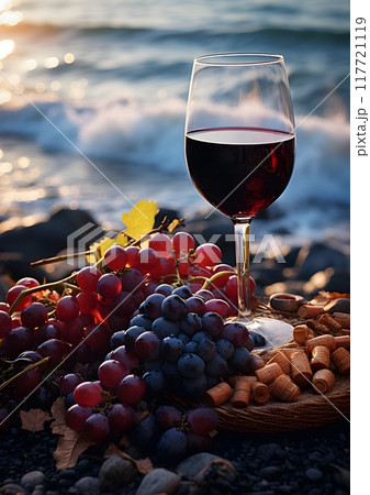 A glass of red wine sits on a sandy beach alongside bunches of grapes, with the ocean waves gently crashing in the background. This scene captures a tranquil and refreshing seaside moment, ideal for u 117721119