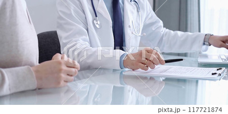 Doctor consulting patient. Male physician is pointing into medical records on a clipboard while talking with a woman in a clinic, close up. Medicine concept Doctor consulting patient. Male physician is pointing into medical records on a clipboard while talking with a woman in a clinic, close up. Medicine concept 117721874