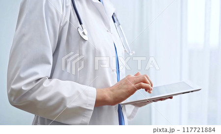 Female doctor using digital tablet in clinic. Healthcare professional with a stethoscope around her neck operating a touch screen computer while standing straight. Medicine and healthcare 117721884