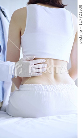 Doctor and patient. Physician wearing white medical gloves examining back of female patient in clinic. Orthopedics and pediatric in medicine 117721939