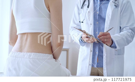 Doctor man is making notes on a clipboard while patient woman is describing back pain. Medicine and orthopedics concepts 117721975