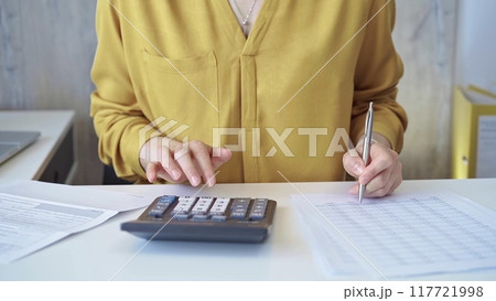 Businesswoman with yellow blues is using dark calculator and taking notes in her office. Taxes and audit in business 117721998