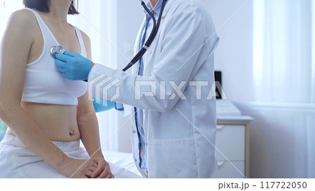 Doctor and patient. Physician wearing blue medical gloves is using stethoscope examining woman lungs in clinic. Medicine concept Doctor and patient. Physician wearing blue medical gloves is using stethoscope examining woman lungs in clinic. Medicine concept 117722050