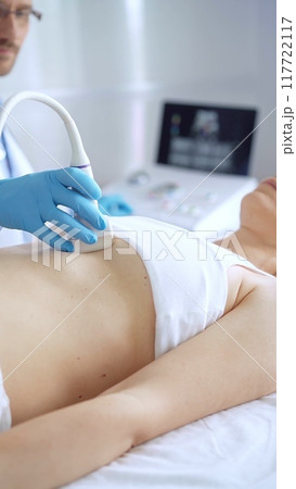 Doctor man wearing blue protective gloves is using ultrasound equipment on the breast of a female patient. Mammary gland health 117722117