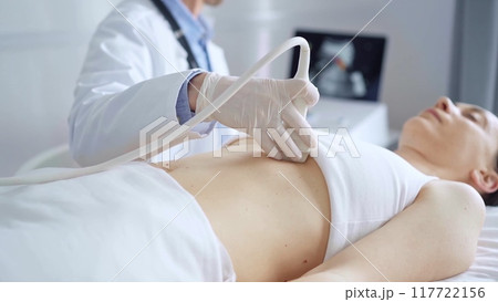 Doctor man, wearing white medical gloves, is using ultrasound equipment on the breast of a female patient lying down for a medical cardiology examination. Medicine concept 117722156