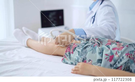 Doctor and kid patient. Orthopedist performing ultrasound examination on a child's knee in hospital. Medicine 117722308