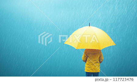 Person in a yellow raincoat holding a yellow umbrella in the rain, rear view, copy space 117723476