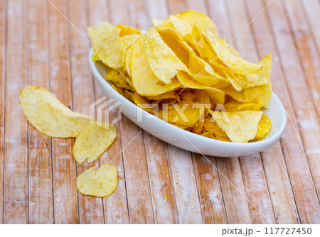 Potato chips in bowl on background. Salty crisps scattered on table 117727450