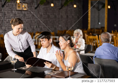 Waitress helps to sort out menu, choose original dish to young married couple 117727503