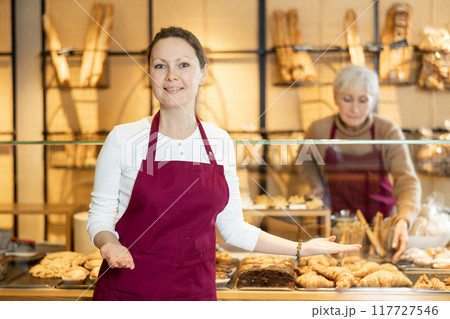 Cheerful female baker welcoming everyone into her bakery Cheerful female baker welcoming everyone into her bakery 117727546