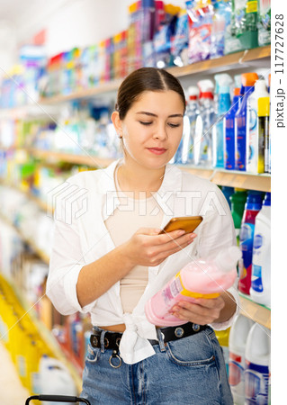 in supermarket, girl carefully scans qr code from label on dish detergent 117727628