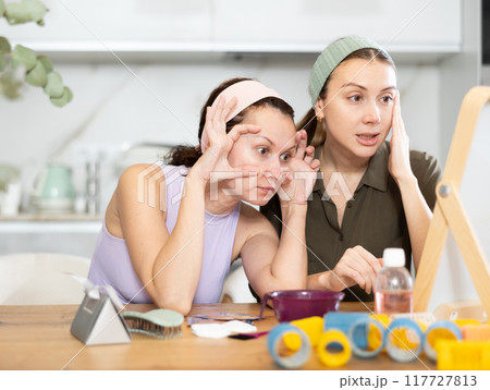 Two women looking at themselves in mirror 117727813