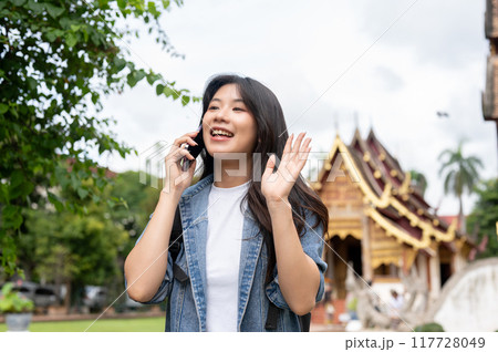A beautiful Asian female tourist is talking on the phone while visiting a temple. 117728049