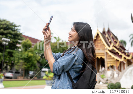 A beautiful, happy Asian female tourist is taking a photo of a temple with her smartphone. 117728055
